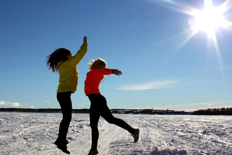 Två personer syns hoppas upp i luften av glädje. Solen skiner från en klarblå himmel och de är på isen på älven.