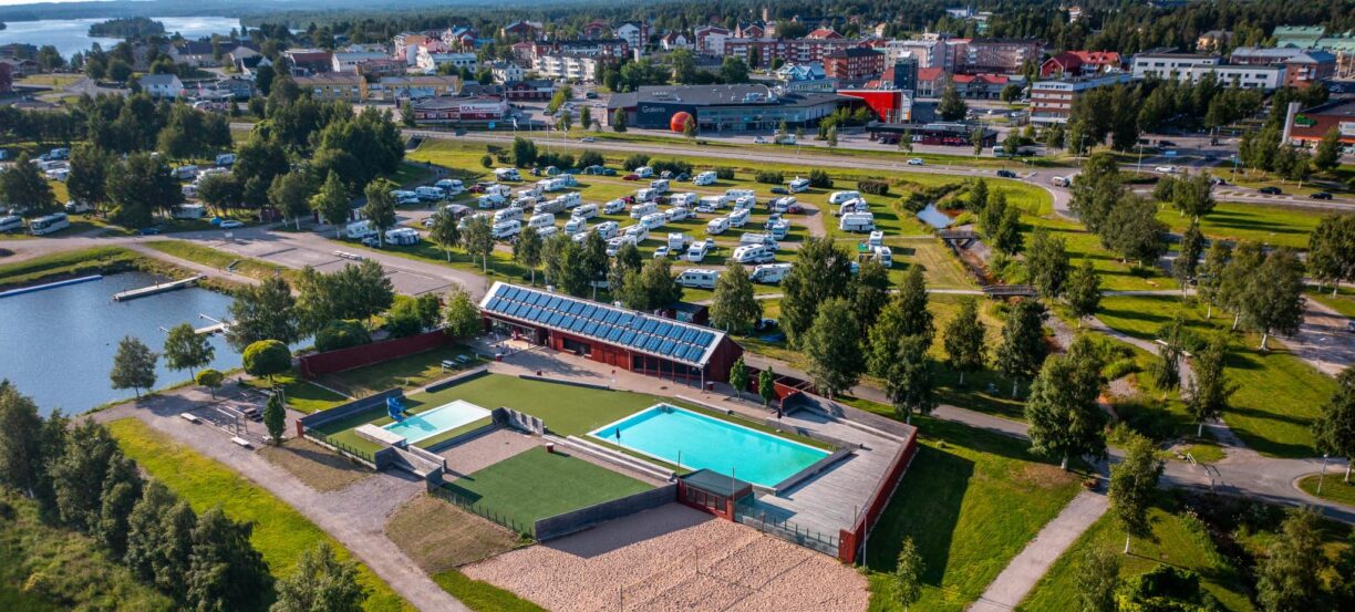 Vybild över Strandängsbadet och Kalix camping med Kalix centralort i bakgrunden. På bilden syns en pool, volleybollbana och flertalet husbilar.