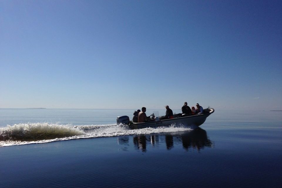 En motorbåt med flertalet människor åker på ett spegelblankt vatten med blå himmel.