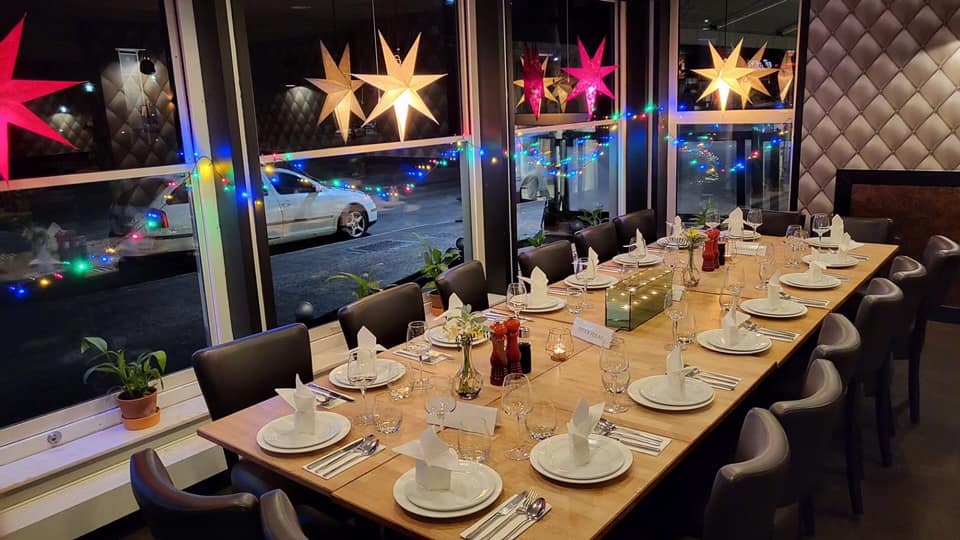 Ett dukat bord med vita tallrikar och vita servetter. Bakom bordet syns en fönstervägg med tända julstjärnor.