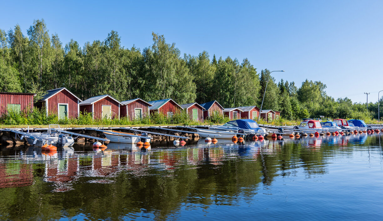 Röda sjöbodar och båtar vid Nyborgs hamn. Spegelblankt vatten och blå himmel.