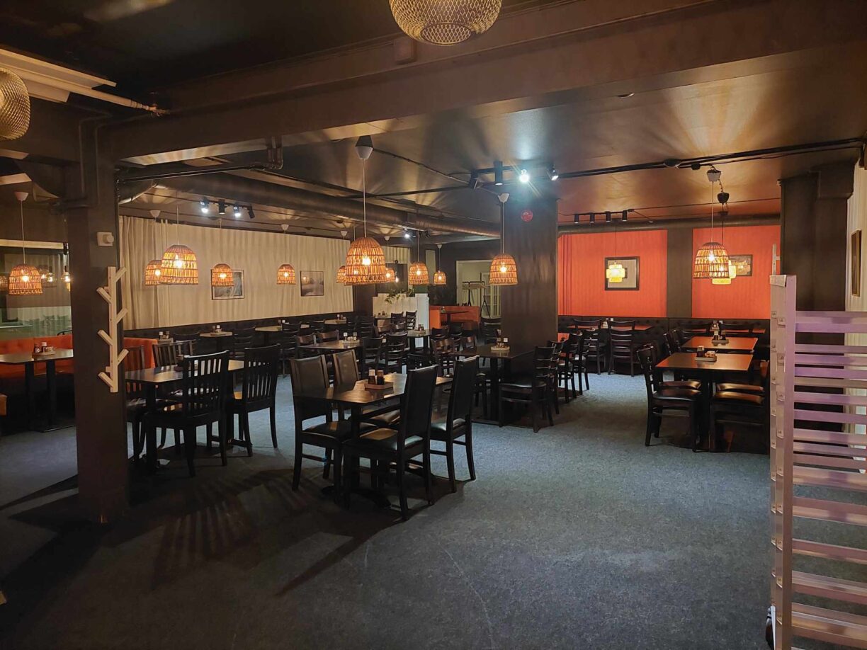 Inifrån Wok of Flames restaurangen där du ser flera mörka bord med stolar. Mörkblått golv med röda detaljer på väggarna och lampor som lyser upp lokalen.