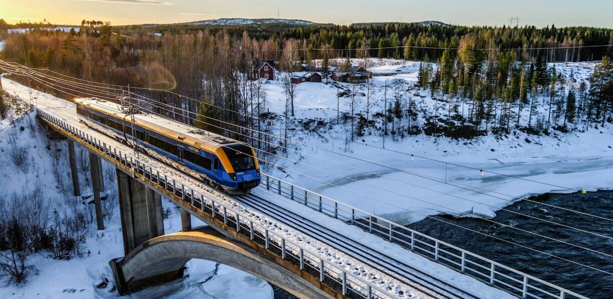 Tåg på en bro över älven i ett snöigt landskap.