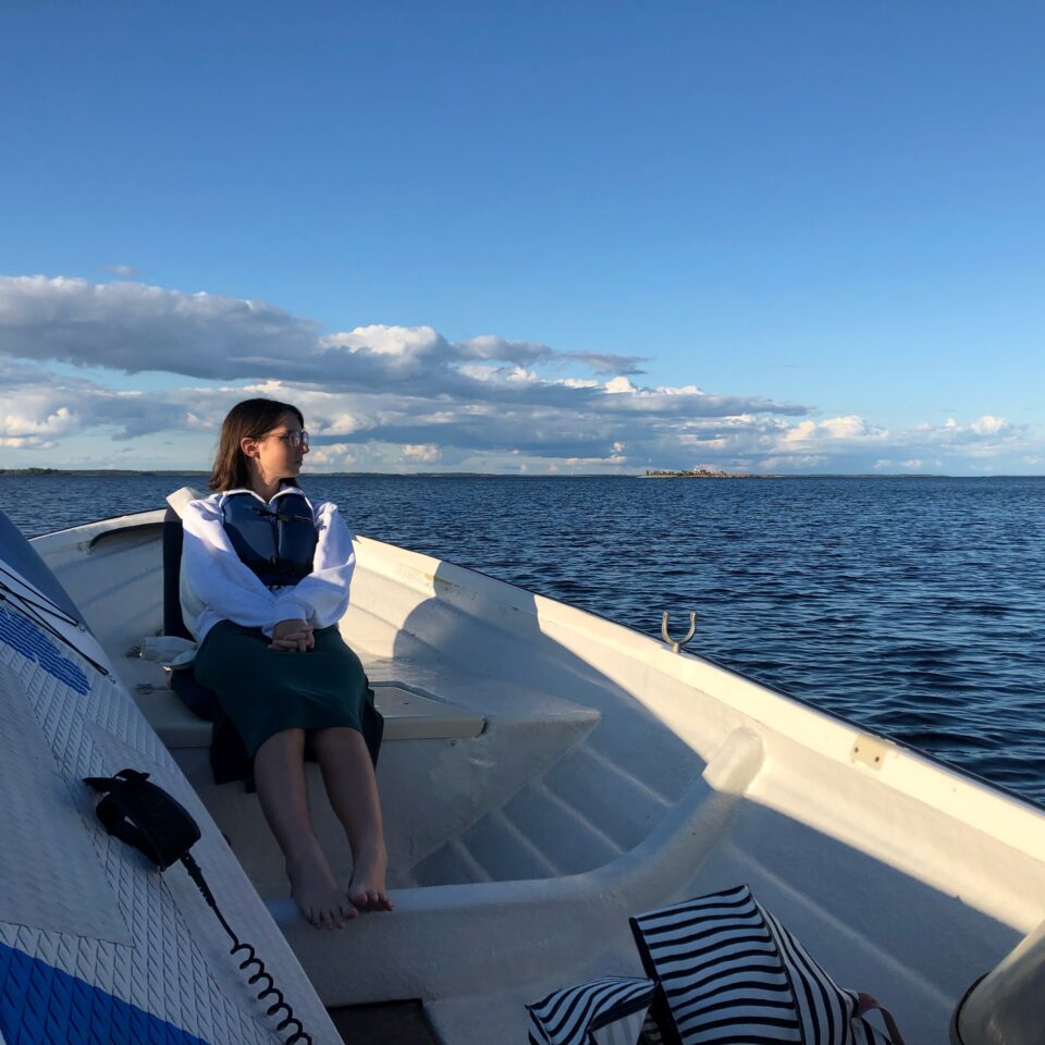 Sara i fören på en båt en solig dag med blå himmel och blått vatten.