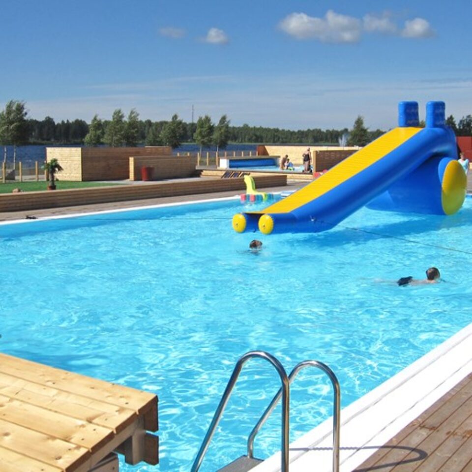 Simbassäng med rutschkana med blå vatten och barn som badar.