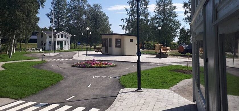 En miniatyr-stad med asfalterad väg, små trähus, lyktstolpar och träd.